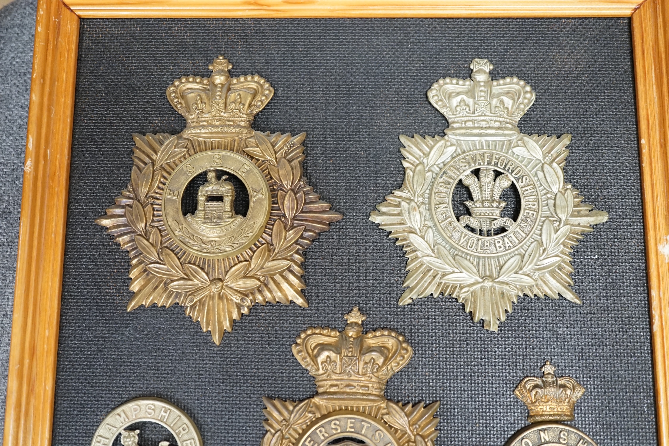 Five military helmet plates and two other centre badges, mounted on a board including; the Essex Regiment, the North Staffordshire 1st Volunteer Battalion, the Somerset Regiment, the Buffs East Kent Regiment, the King’s